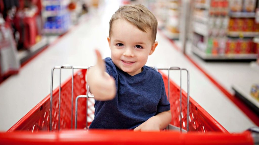 little boy giving thumbs up and holding candy while in a red shopping cart at target store