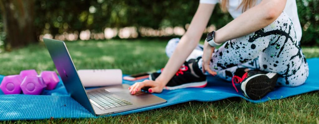 woman sitting on yoga mat in grass yard in the shade using macbook