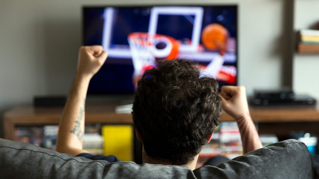 man watching basketball on his new TV he bought on Black Friday at a major discount! Find more TV deals this Black Friday on Slickdeals!